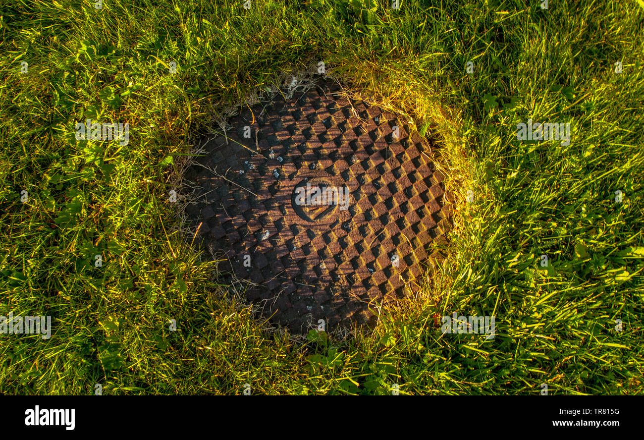A rusty manhole cover in the middle of a grass field. Stock Photo