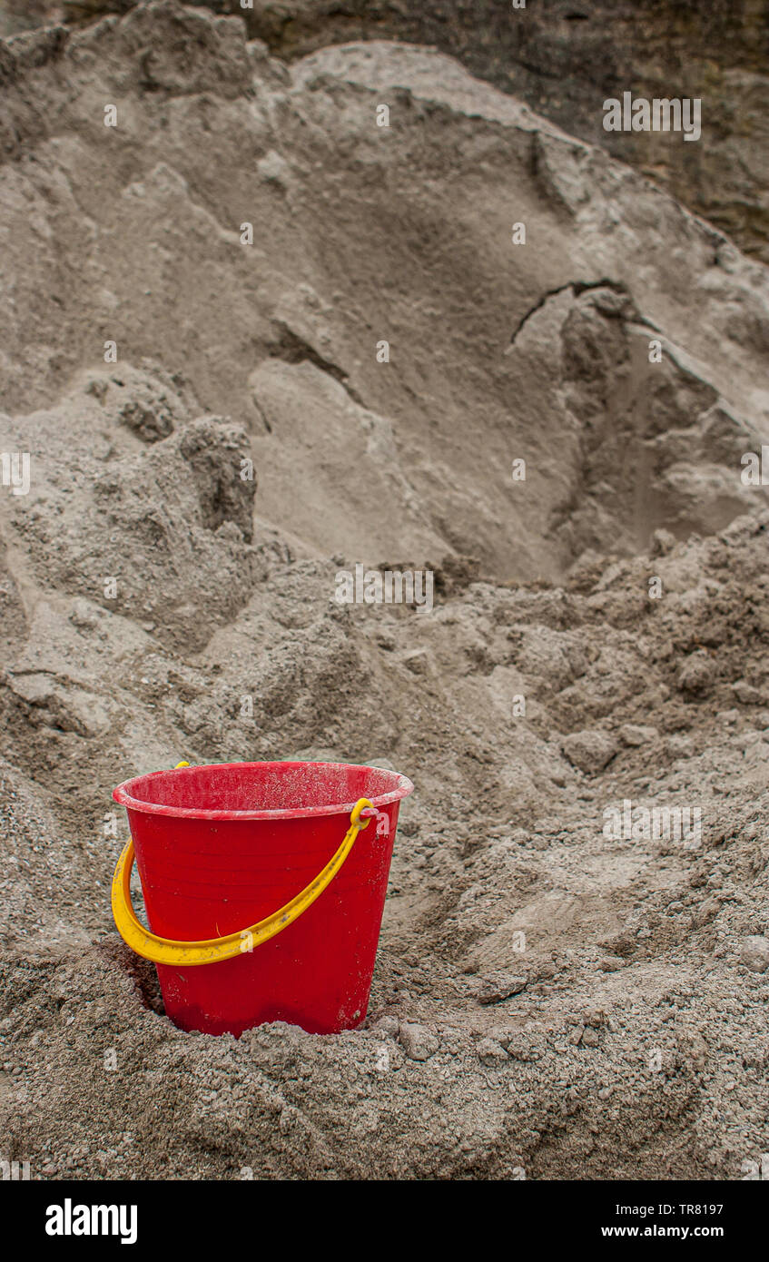 Red plastic bucket in a big pile of sand. Stock Photo