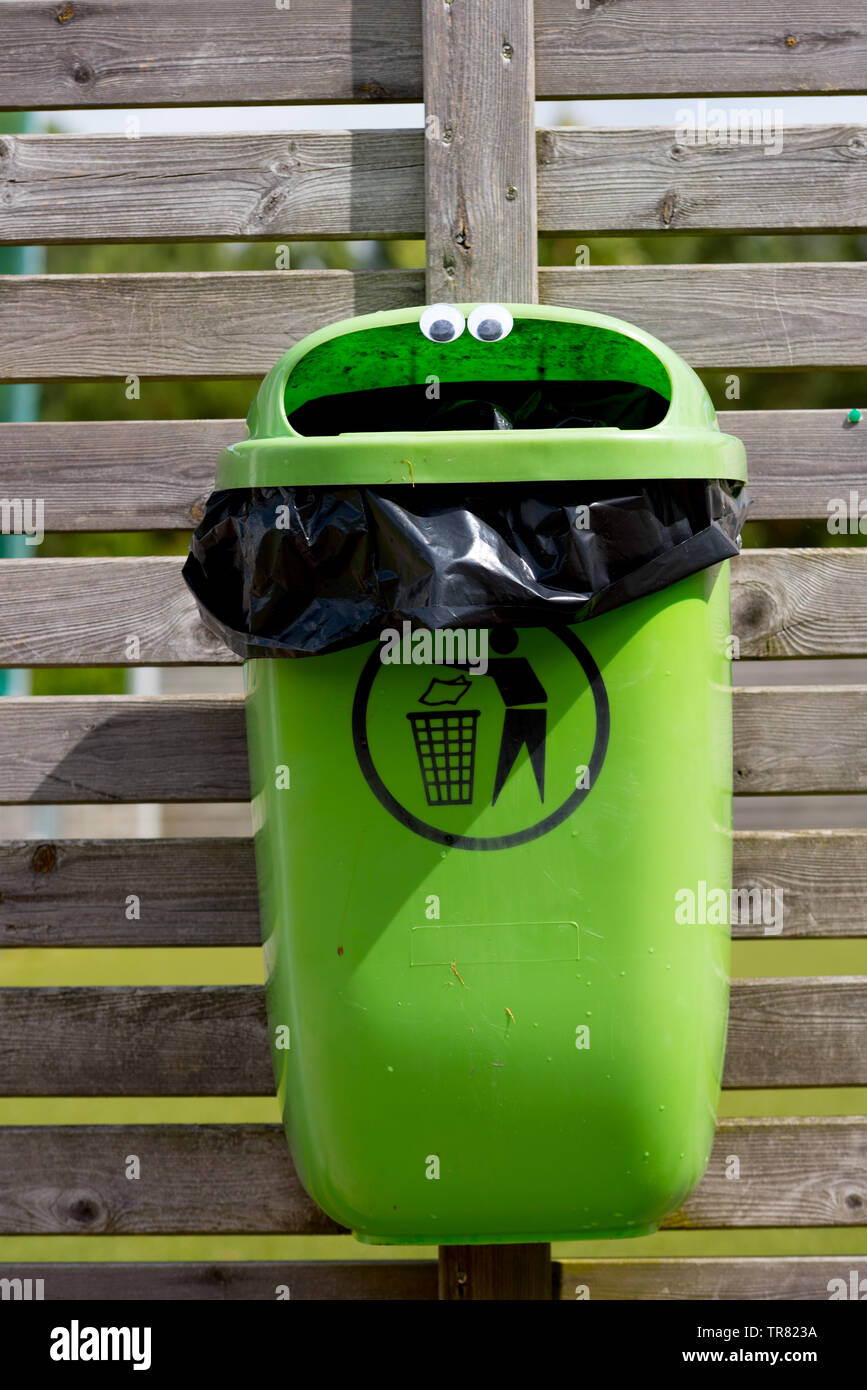 googly eyes on a green trash can mounted on a wooden fence Stock Photo