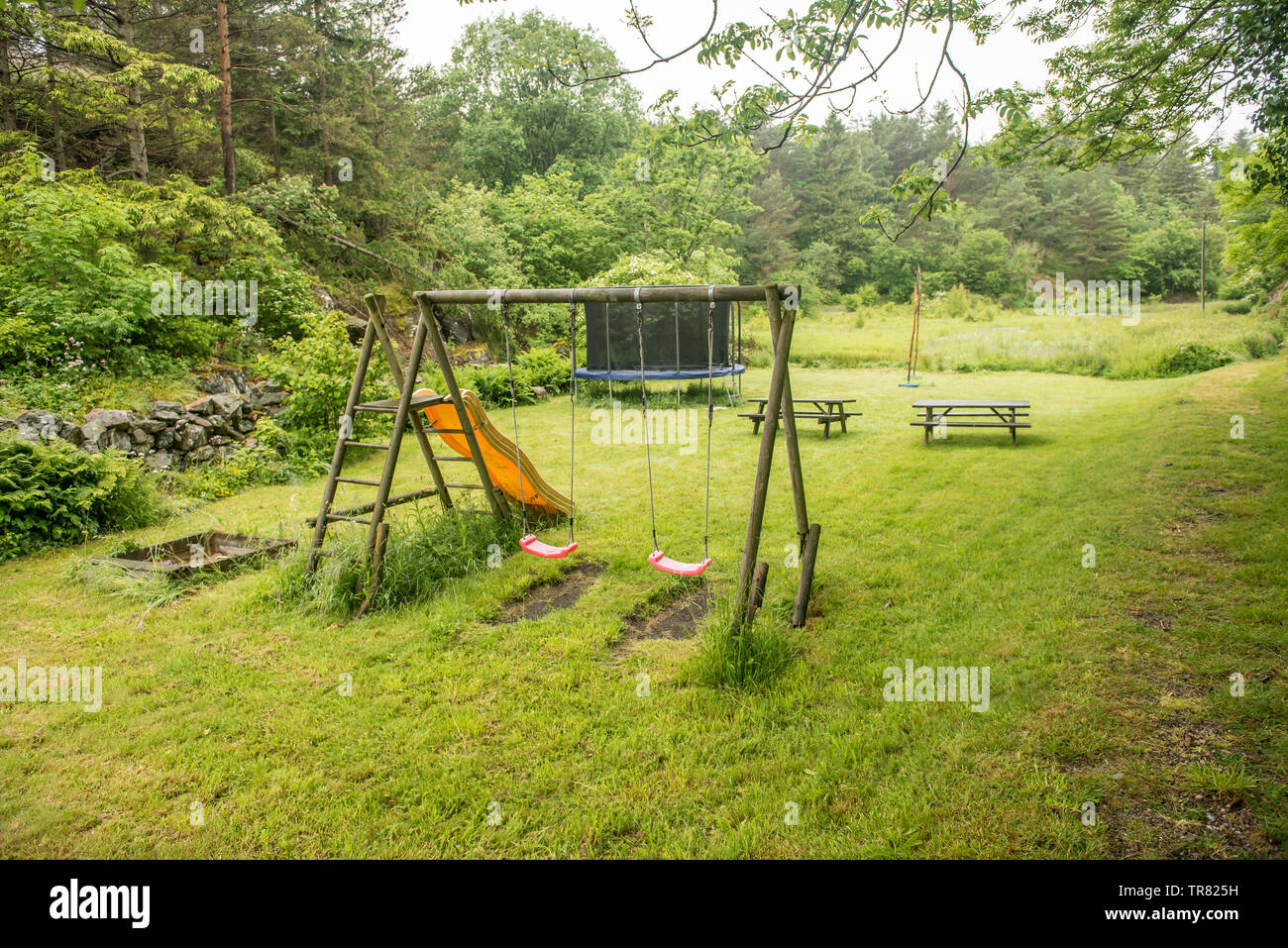A small playground with swings, benches and a trampoline. Stock Photo