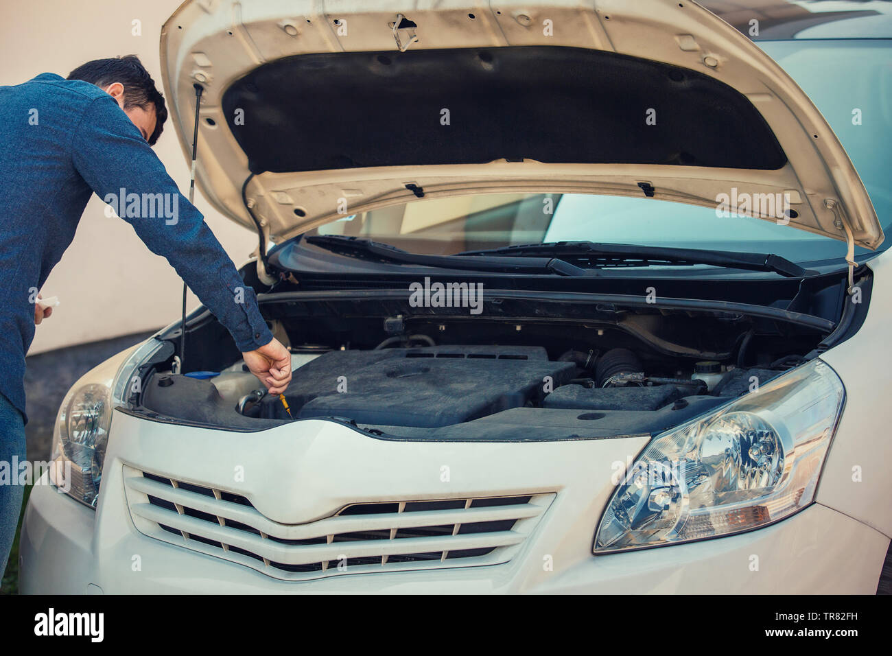 Driver check oil level in the car engine. Vehicle repair service, auto mechanic job. Young man motorist has problems, looking under his car hood for a Stock Photo