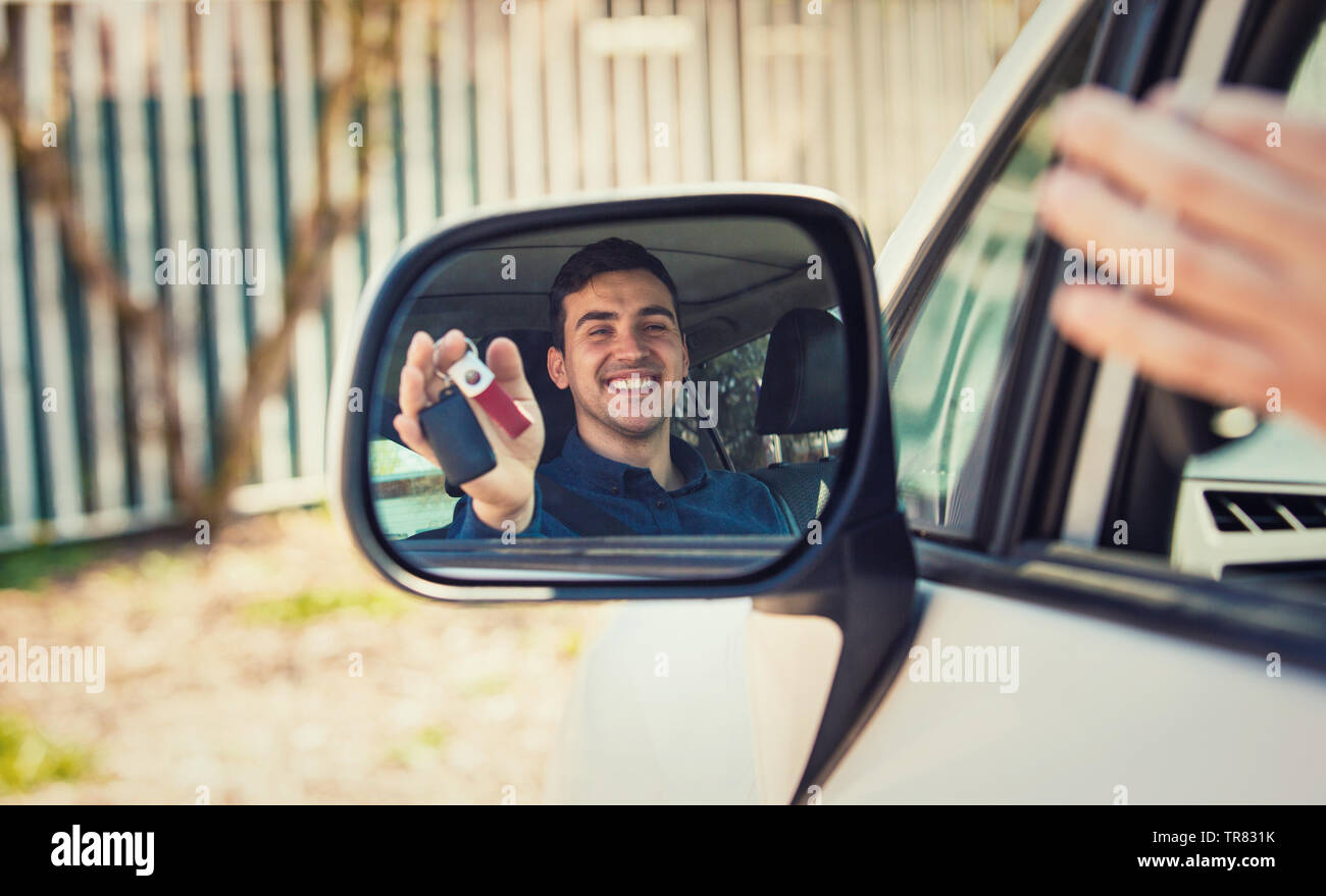 Casual guy driver showing car keys in the side view mirror reflection