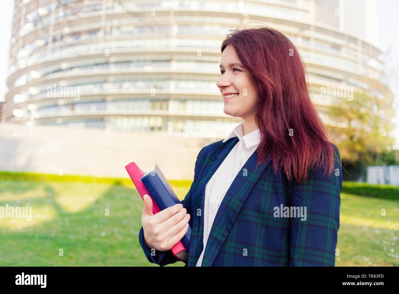Student girl outdoor in campus smiling happy going back to university. Caucsian female college or university student. Caucasian young woman holding bo Stock Photo