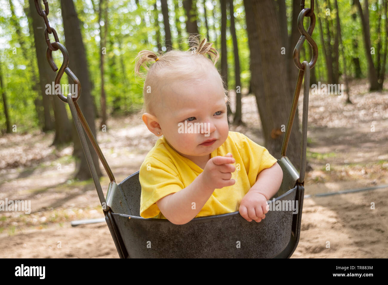 adorable blond caucasian toddler in the swing at the playground Sorel-Tracy pointing finger Stock Photo