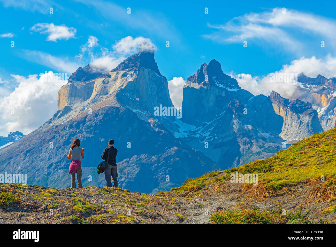 Two tourists, a woman and a man, by the Andes peaks of Cuernos del Paine at sunset, Torres del Paine national park, Puerto Natales, Patagonia, Chile. Stock Photo