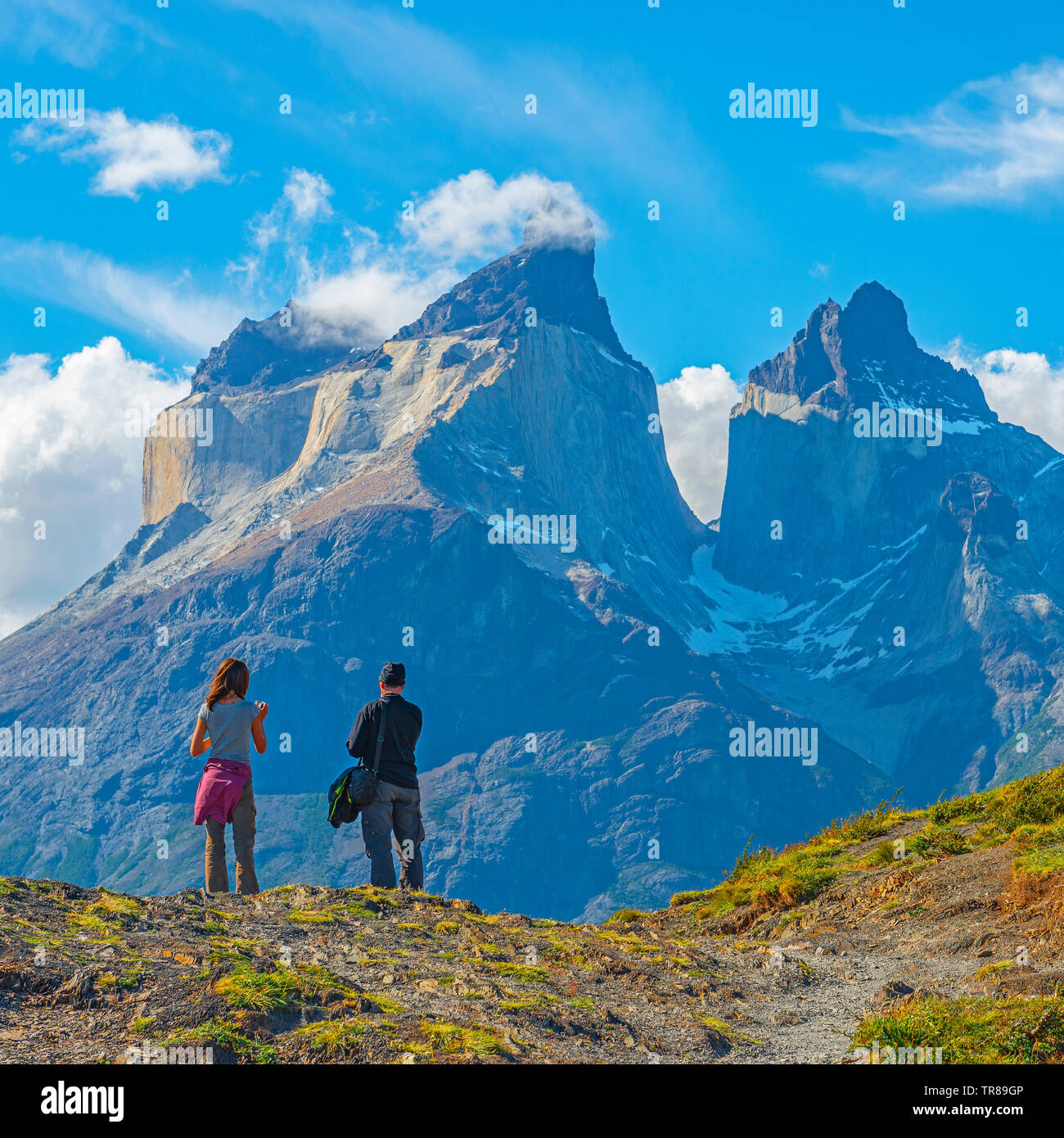 Two tourist, man and woman, looking to the Andes peaks of Cuernos del Paine, Torres del Paine national park, Puerto Natales, Patagonia, Chile. Stock Photo
