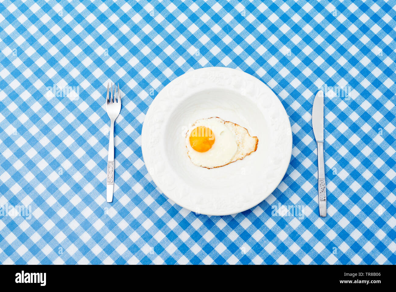 White plate with single fried egg on blue and white pattern tablecloth Stock Photo