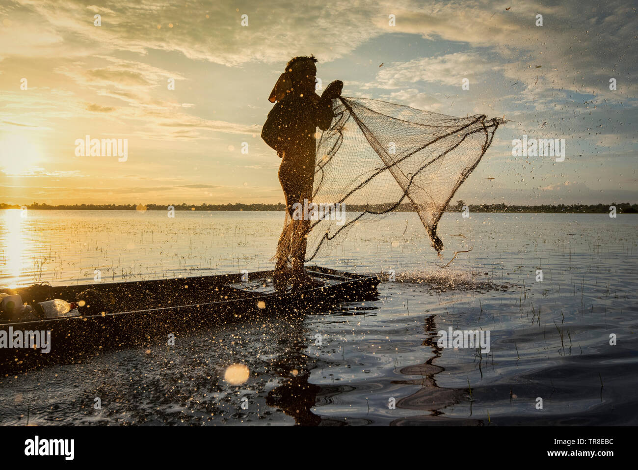 Asia fisherman using net fishing on wooden boat casting net sunset