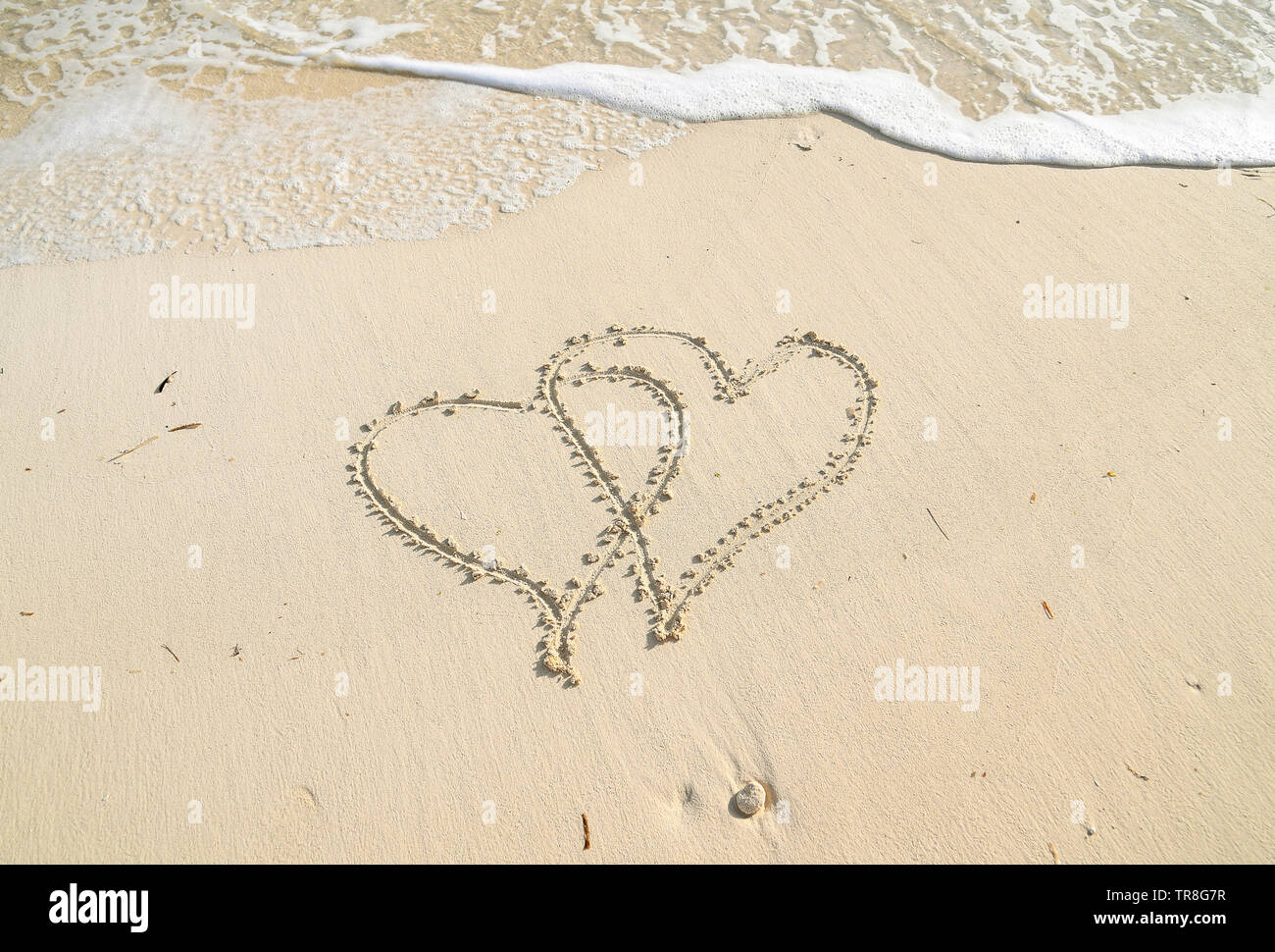 pair of connected heart symbols in beach sand with white frothy ocean surf Stock Photo