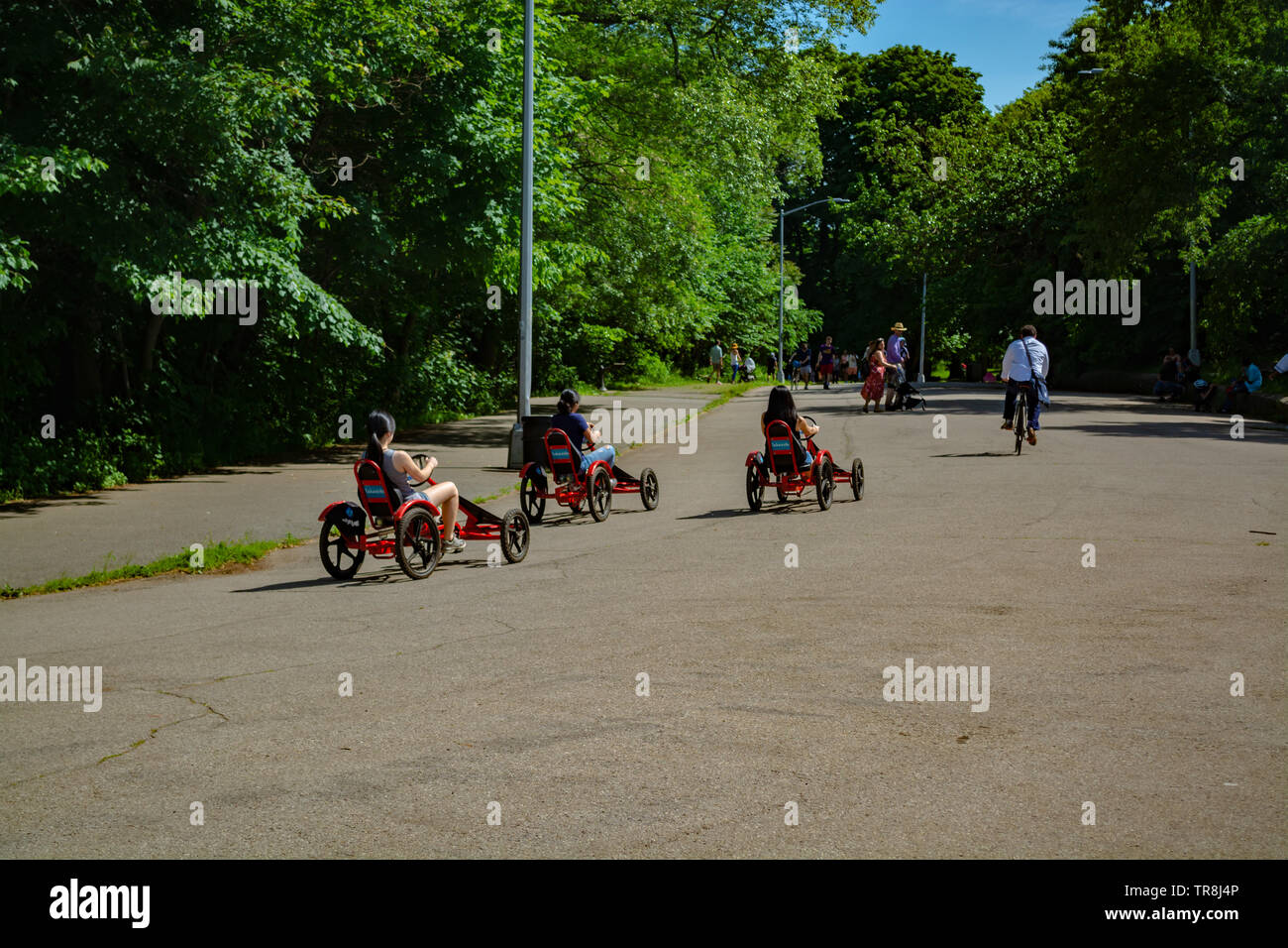 Three Asian young girls are pedaling tricycles on the park road. Stock Photo