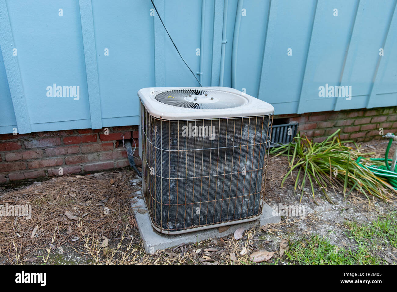 Old air conditioner system compressor next to home, needing maintenance. Stock Photo