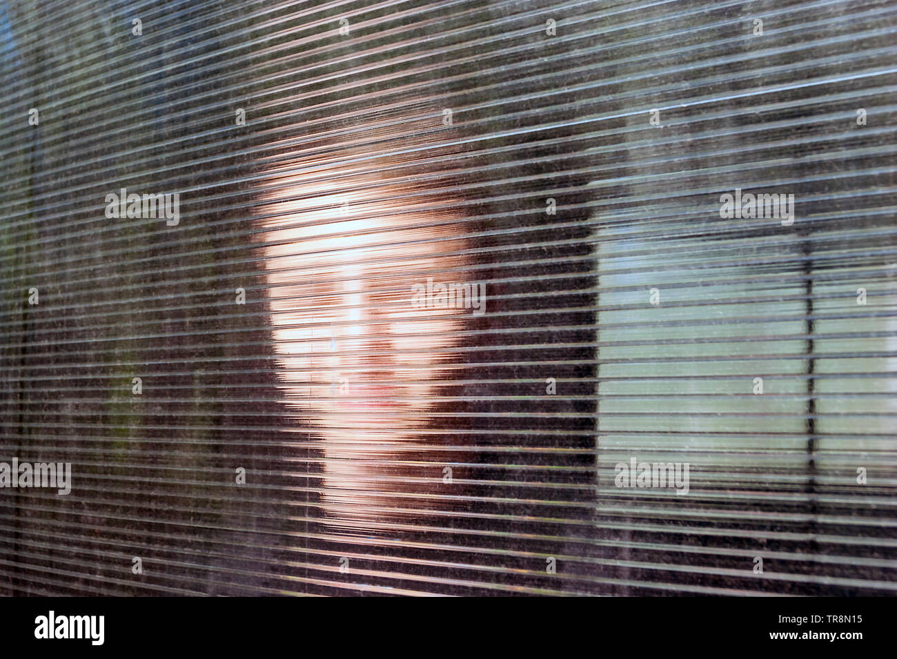 Blurred Smiling Young Face behind Dusty Fluted or Ribbed Glass, Clear Polycarbonate Corrugated Sheet. Online Anonymous, Anon Communication, Data Secur Stock Photo