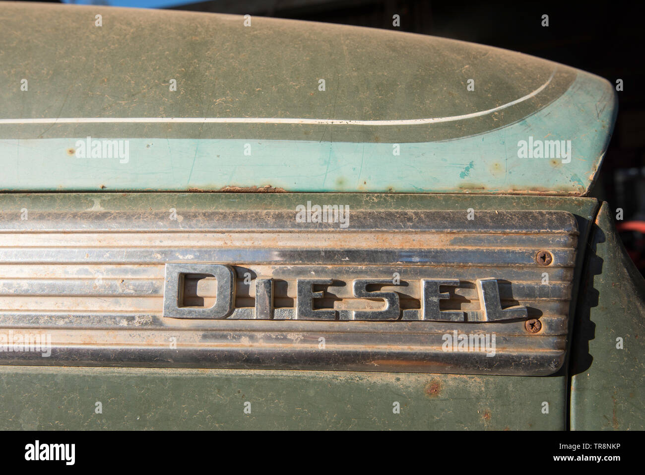 The word Diesel, slightly out of alignment, in raised chrome lettering on the side of an old dusty truck in morning sunlight Stock Photo