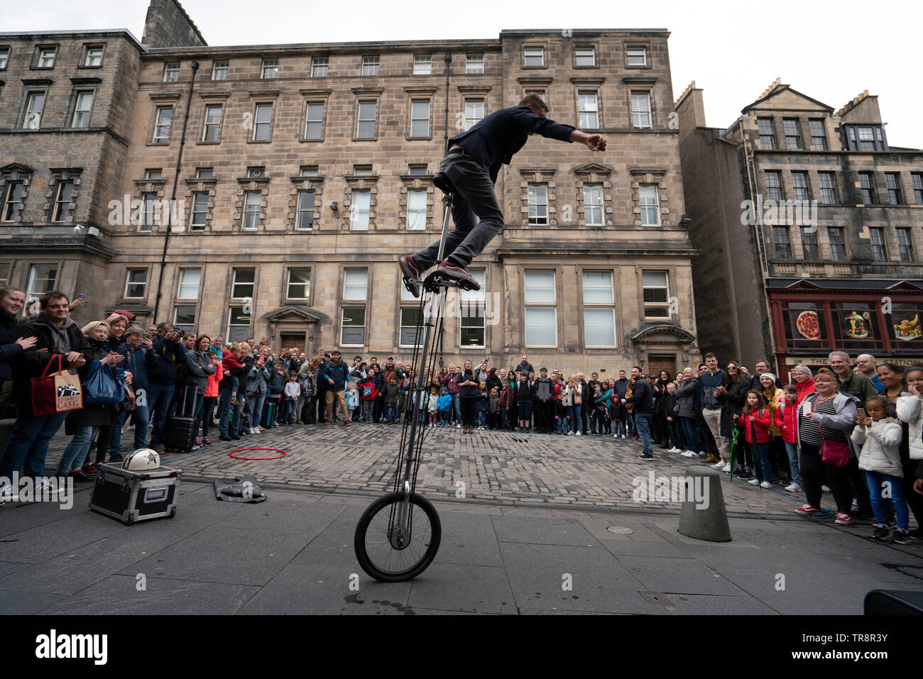 Street performer on unicycle performs to crowd on the High Street Royal Mile in Edinburgh Old Town, Scotland, UK Stock Photo