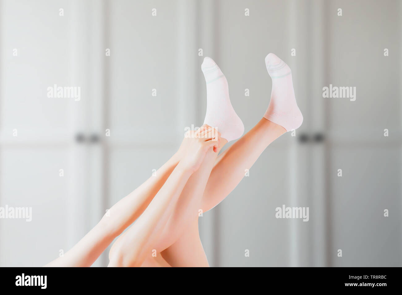Hand Wear White Sock of Woman at Home Wardrobe and Bed in the Morning. Side View of Beautiful Young Female Wearing Bright Cotton Fabric Socks. Stock Photo