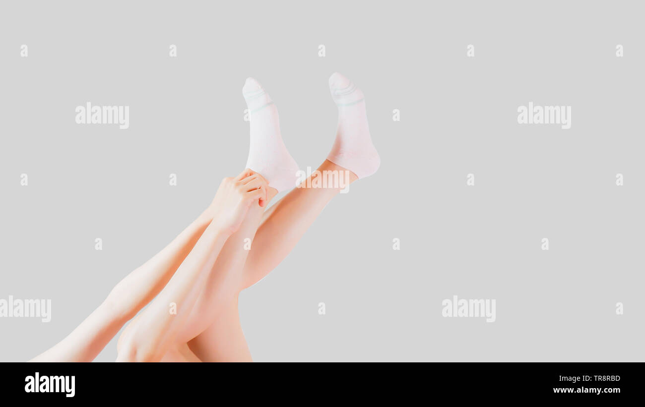 Hand Wear White Sock of People on Grey Studio Light. Side View of Beautiful Young Woman Wearing Bright Cotton Fabric Socks on Gray Color Background. Stock Photo