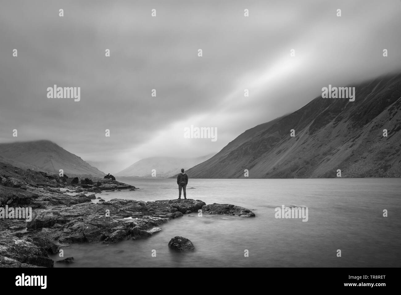 Lone figure in landscape image of Wast Water in UK Lake District during moody Spring evening in black and white Stock Photo