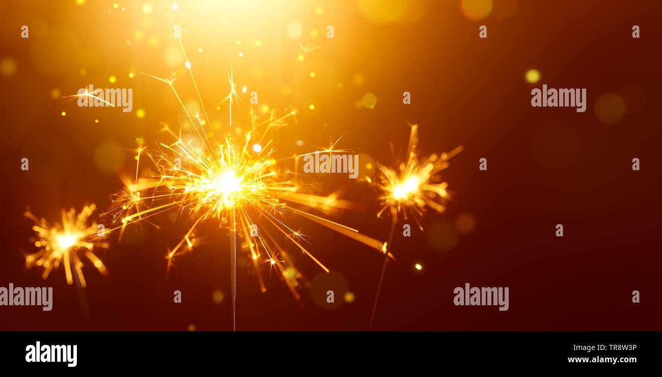 Glittering burning sparkler against golden bokeh background Stock Photo