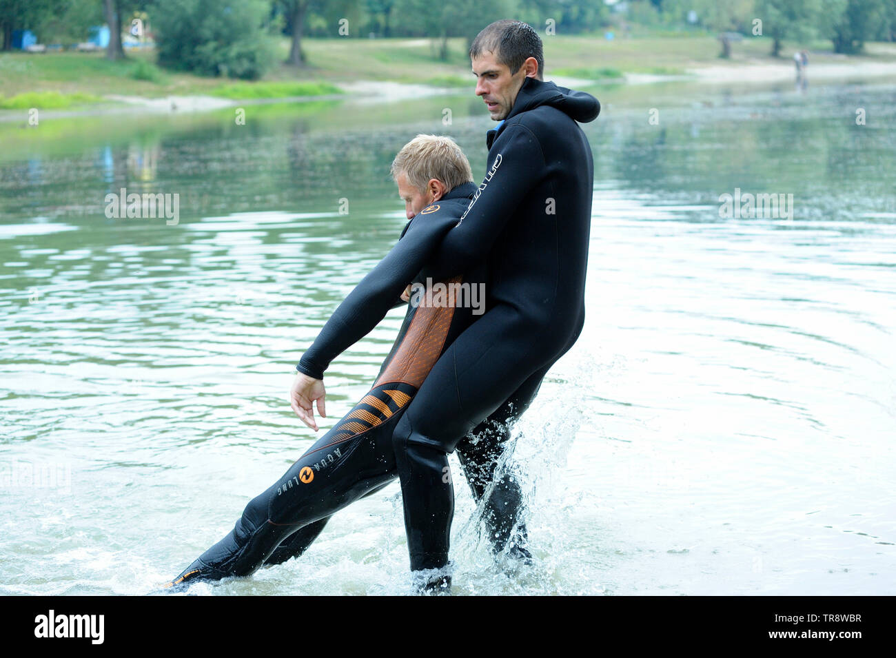 Men in a wet diver suit (lifeguards) showing right way of pulling drowning out from the water. August 10,2018. Kiev, Ukraine Stock Photo
