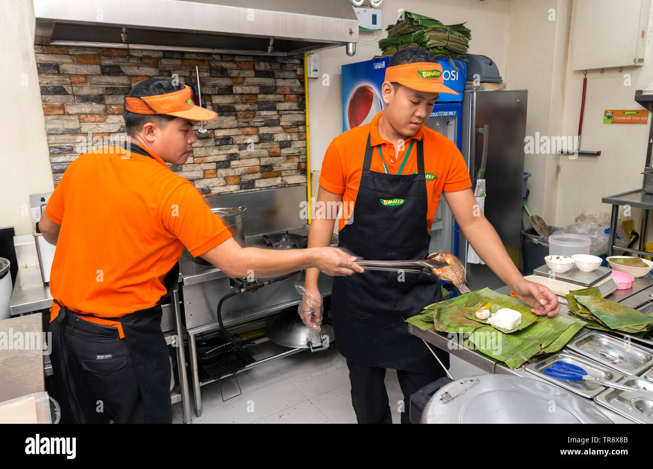 Manila, Philippines - July, 26, 2016: Two young men serving food in a filipino restaurant kitchen in Manila Stock Photo