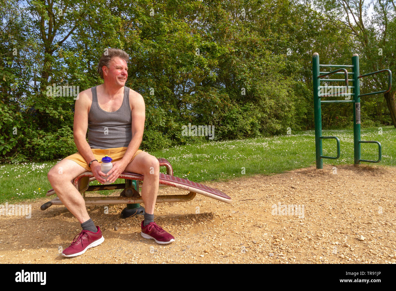 Older (fifty plus) man resting whilst working out on outdoor gym equipment. Healthy outdoors lifestyle concept. Stock Photo