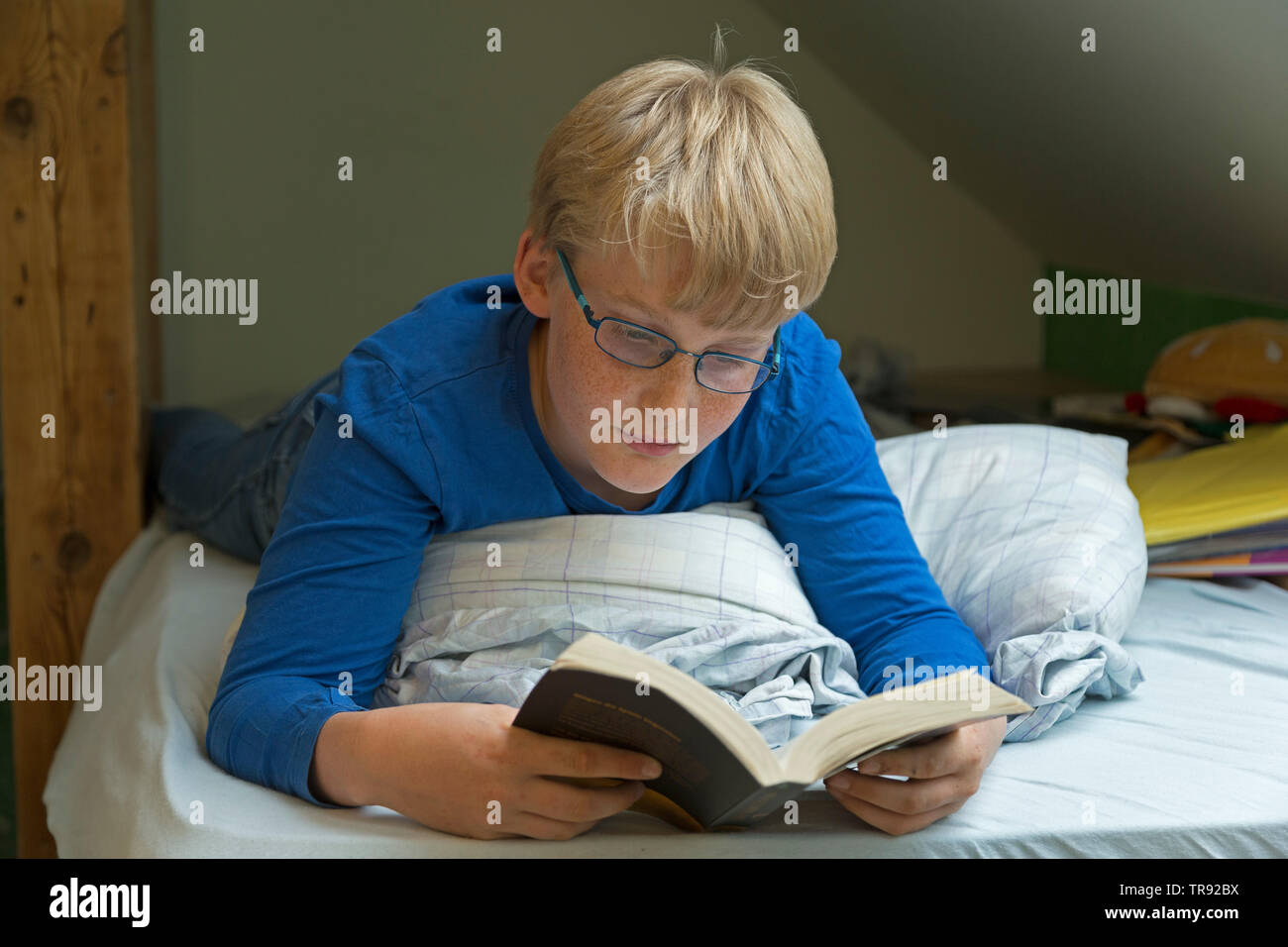 boy lying on his bed reading a book, Germany Stock Photo