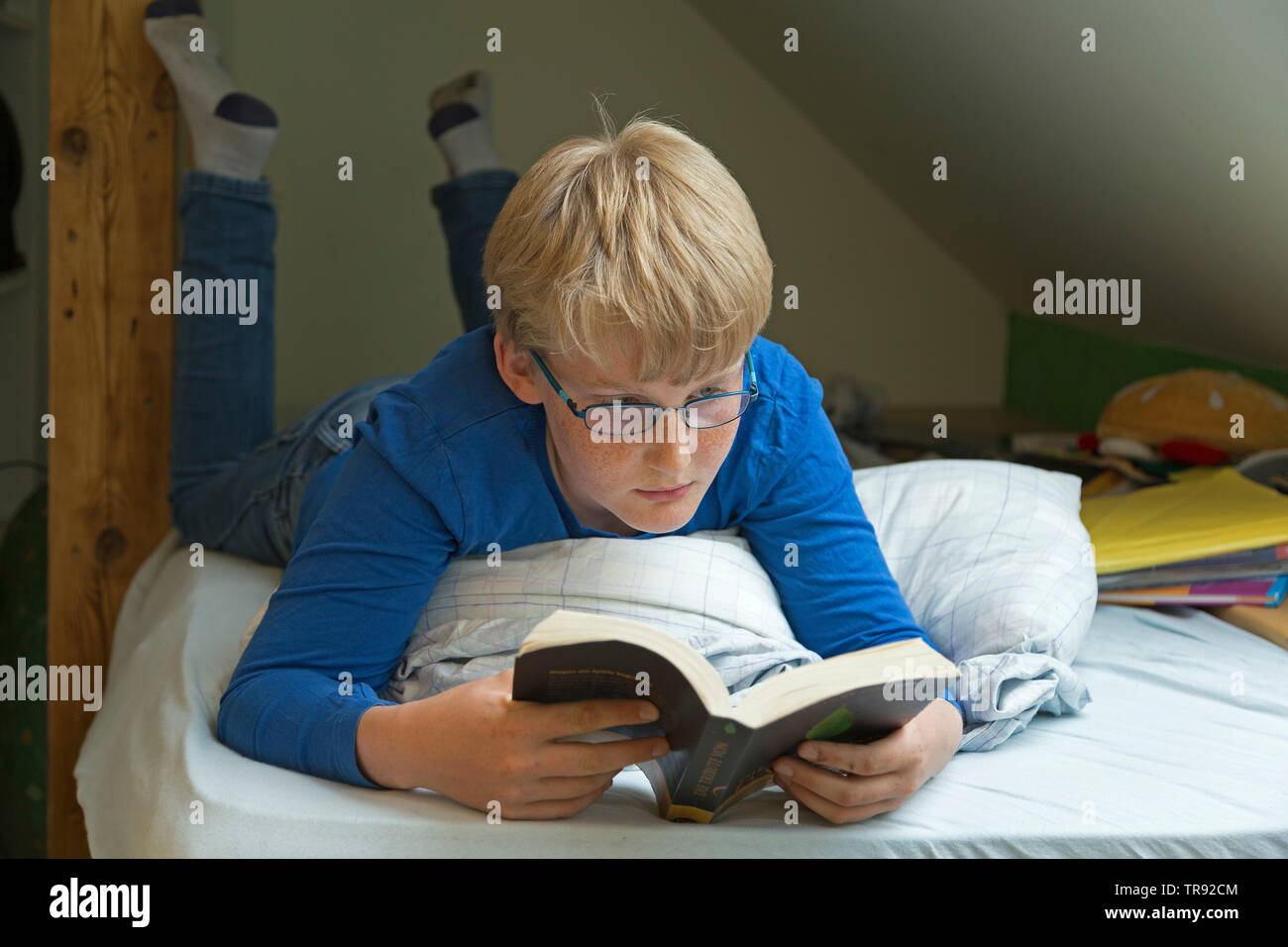 boy lying on his bed reading a book, Germany Stock Photo