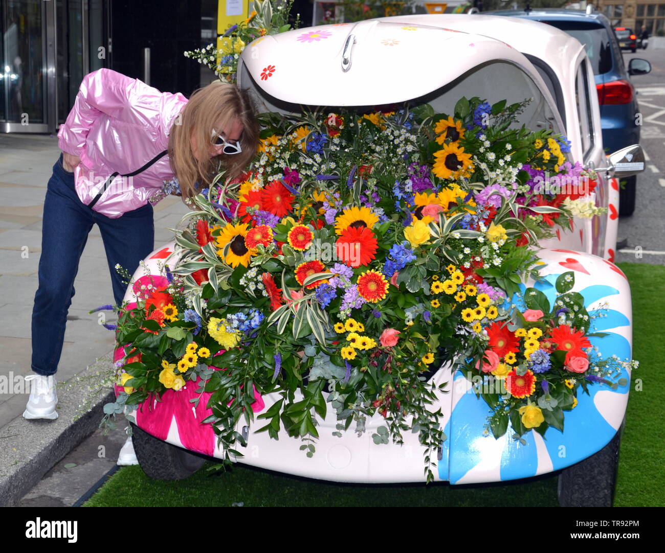 The Manchester Flower Show, part of Manchester's King Street  Festival on June 1st - 2nd, 2019, prepares to open. This year’s theme:Flower Power! Retro objects, like this Volkswagen beetle car, feature in the festival. A female visitor to the city looks at the flowers. Stock Photo