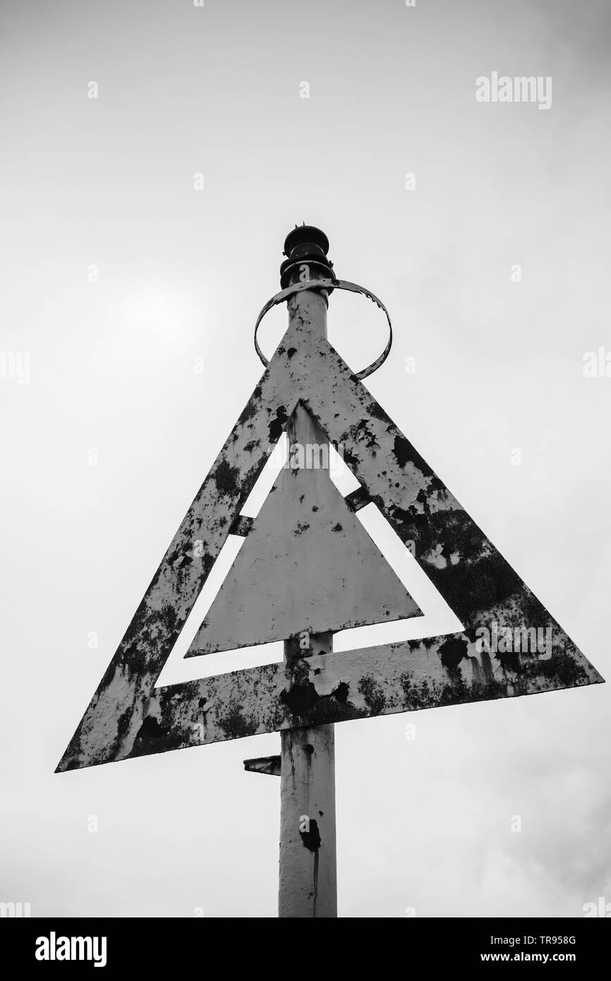 Rusty triangular navigation mark under gray cloudy sky, black and white photo Stock Photo