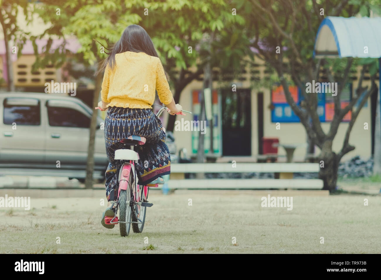 Back view of female teacher rides bicycle to teach students at ...