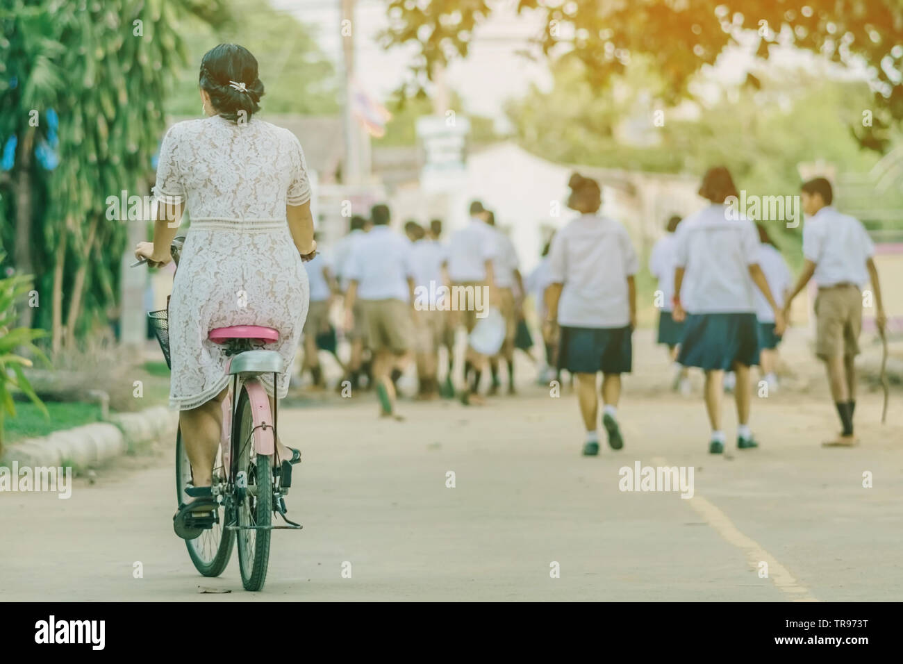 Back view of female teacher rides bicycle to teach students at ...