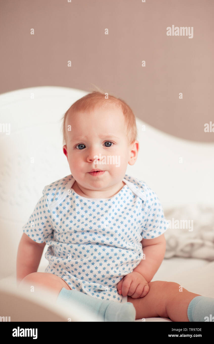Cute baby boy 1 year old sitting in bed in room. Looking at camera