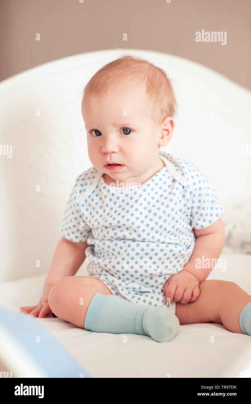 Funny baby boy sitting in bed in room. Looking at camera. Childhood