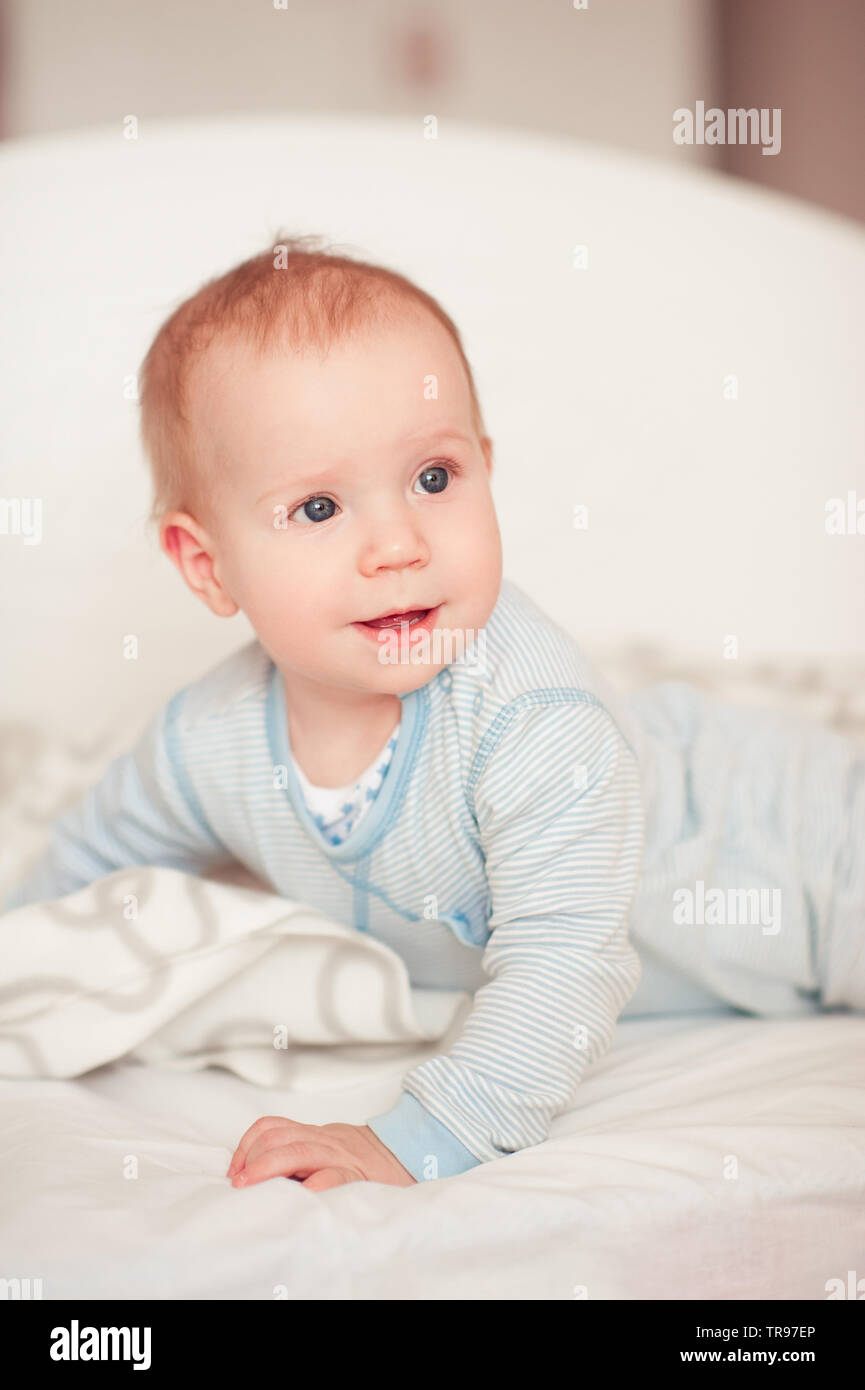Smiling baby boy wake up in bed in room. Wearing pajamas. Looking away. Good morning. Stock Photo
