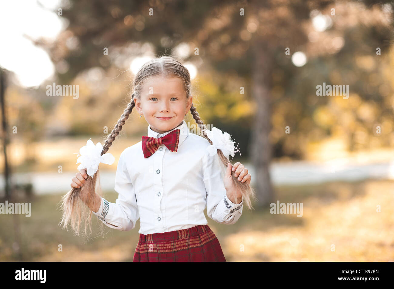 Smiling pupil girl 6-7 year old posing outdoors wearing school uniform. First grade. Back to school. Stock Photo