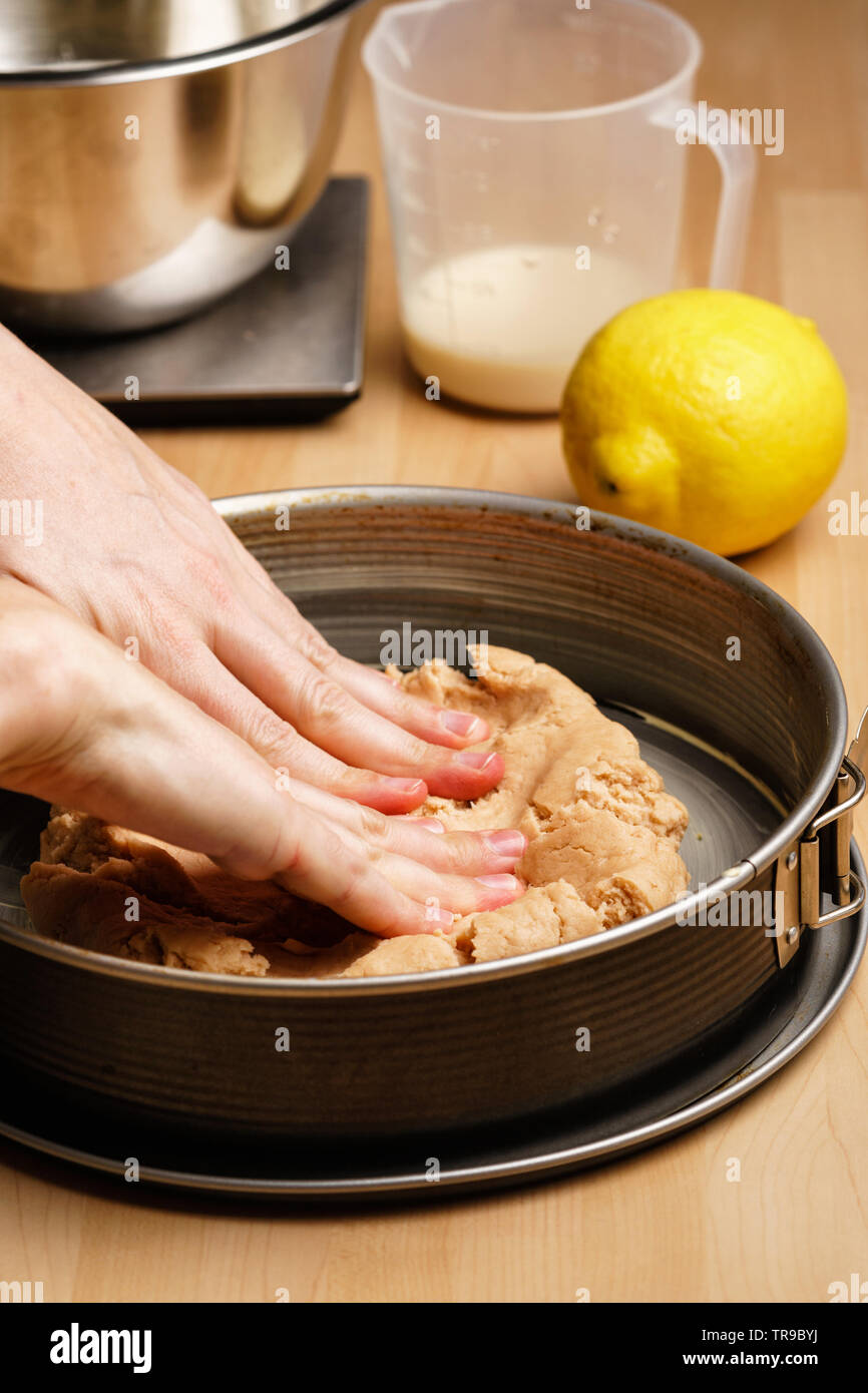 Two female caucasian hands spread out the raw dough in a black baking pan, baking utensils in the background - side view, portrait orientation Stock Photo