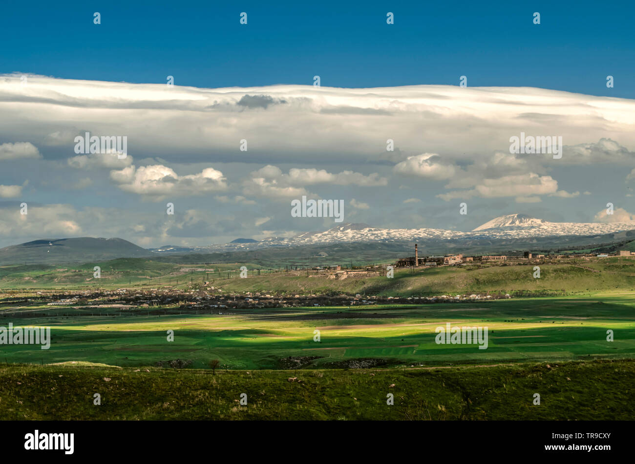A huge turbulent cloud with Cumulus clouds hung in the blue sky over the valley and villages on the background of the mountains of Gegham ridge in Arm Stock Photo