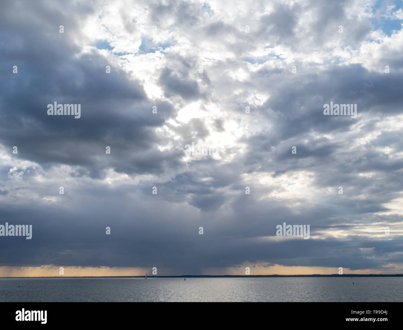 a rainfront moving approaching over Solent with lone single yacht sailing in sea with buoy under big sky storm clouds orange sunset Stock Photo