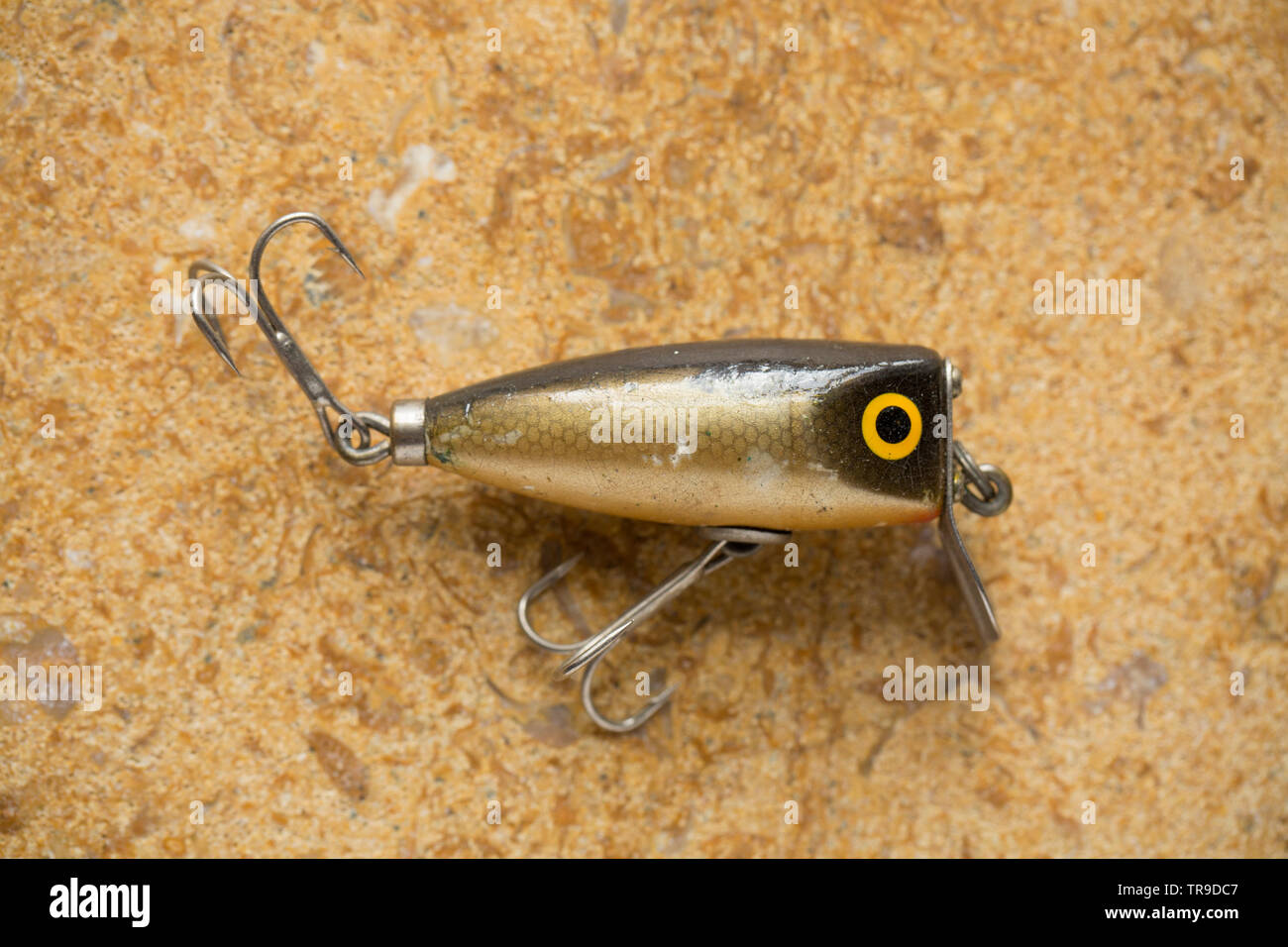 A vintage fishing lure equipped with treble hooks photographed on a stone background. These type of lures are often called plugs and are designed to c Stock Photo