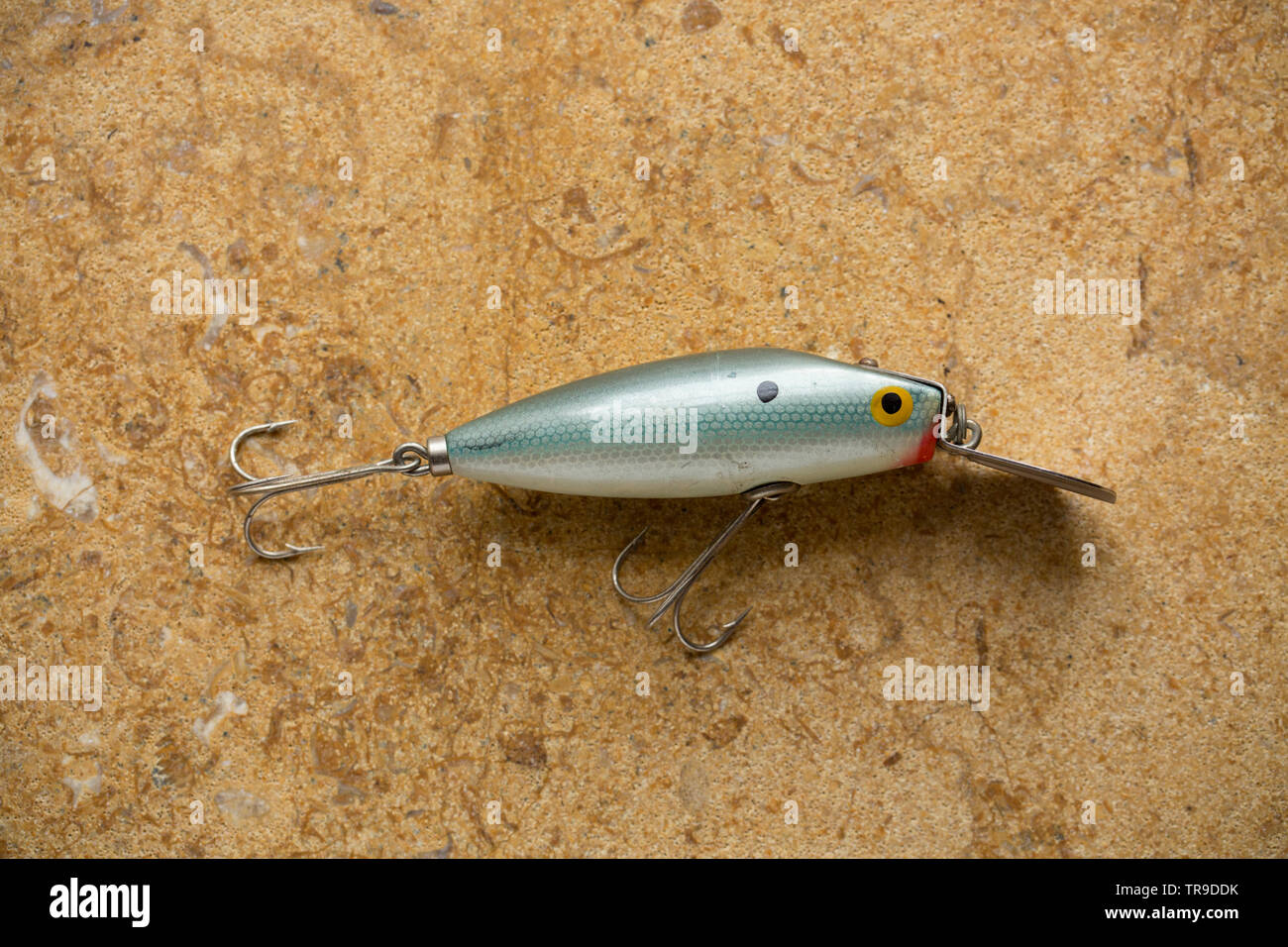 A vintage fishing lure equipped with treble hooks photographed on a stone background. These type of lures are often called plugs and are designed to c Stock Photo