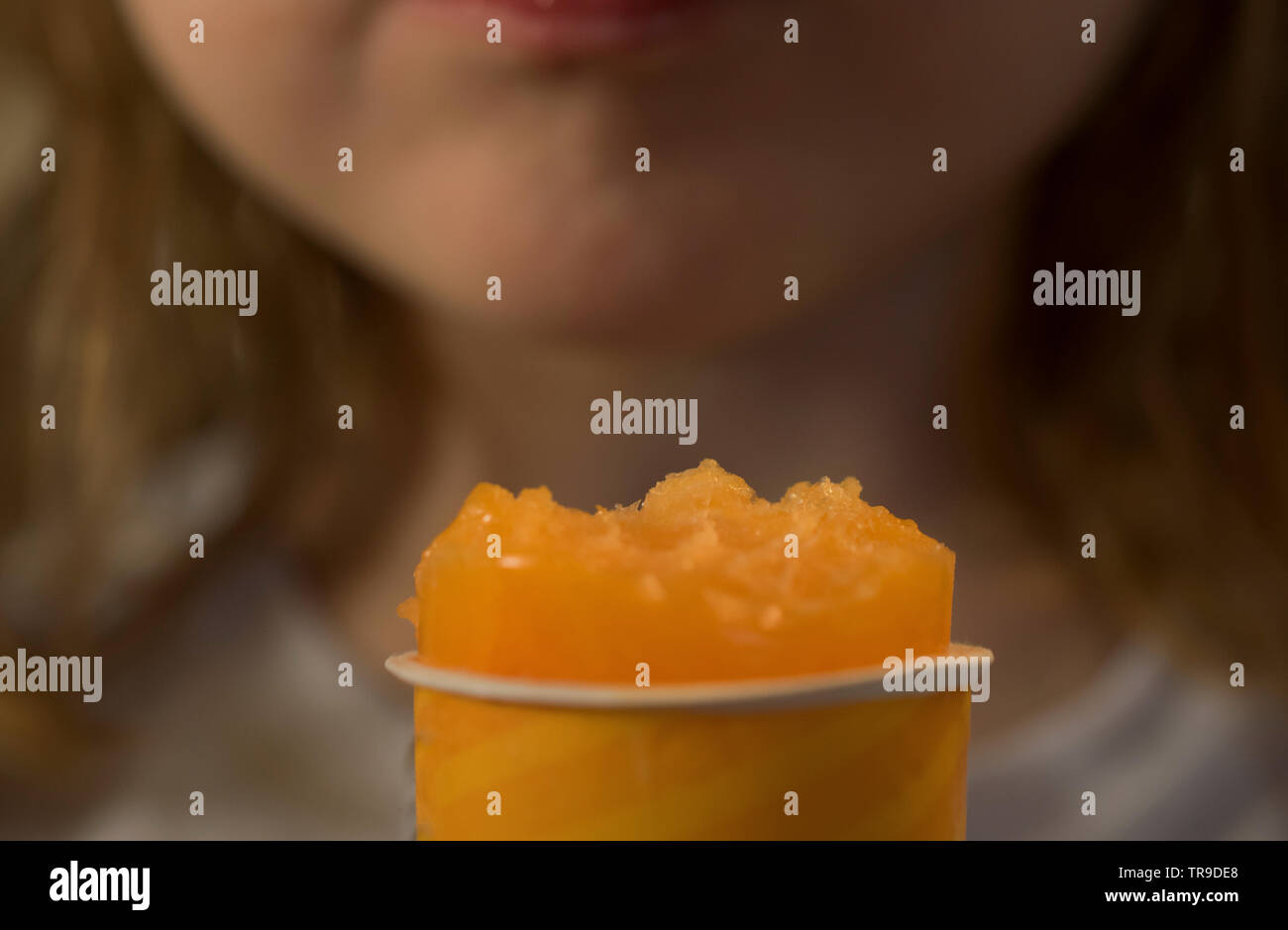 A close-up of a girl eating an orange ice cream Stock Photo