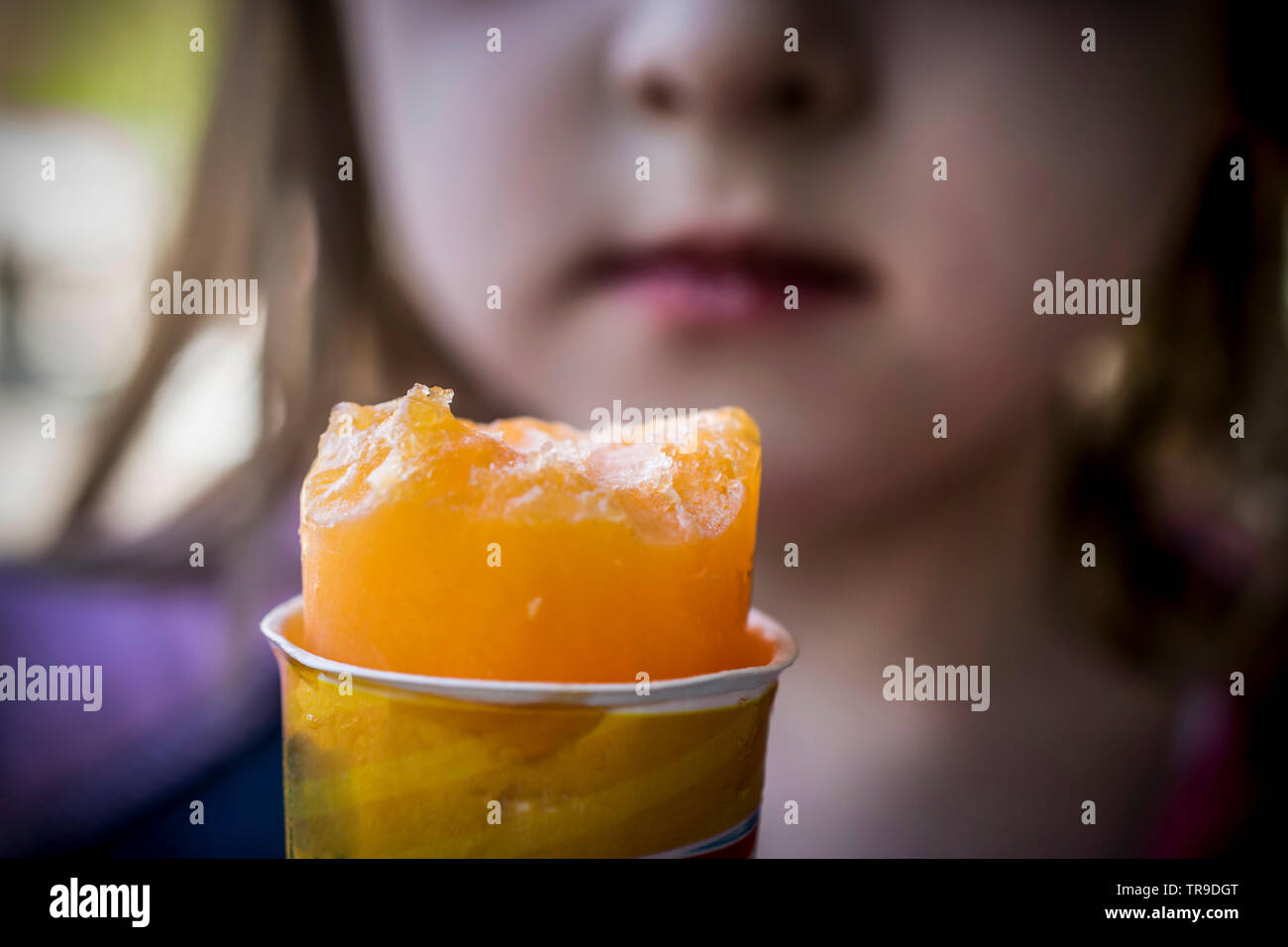 A close-up of a girl eating an orange ice cream Stock Photo