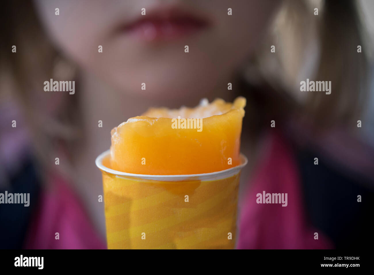 A close-up of a girl eating an orange ice cream Stock Photo