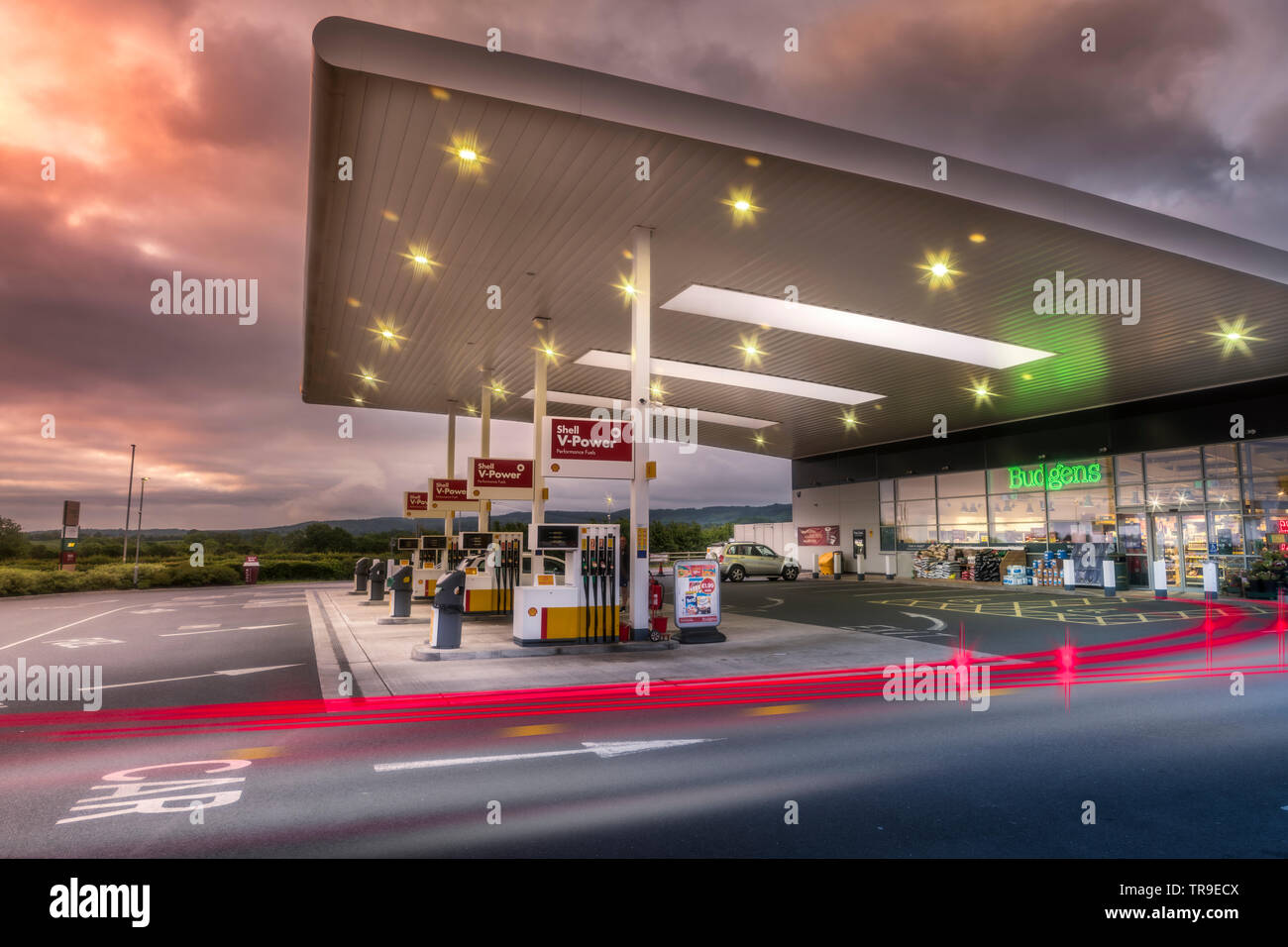 At dawn, vehicles pull onto a garage forecourt, as the sun illuminates storm clouds gathering in the sky above. Stock Photo