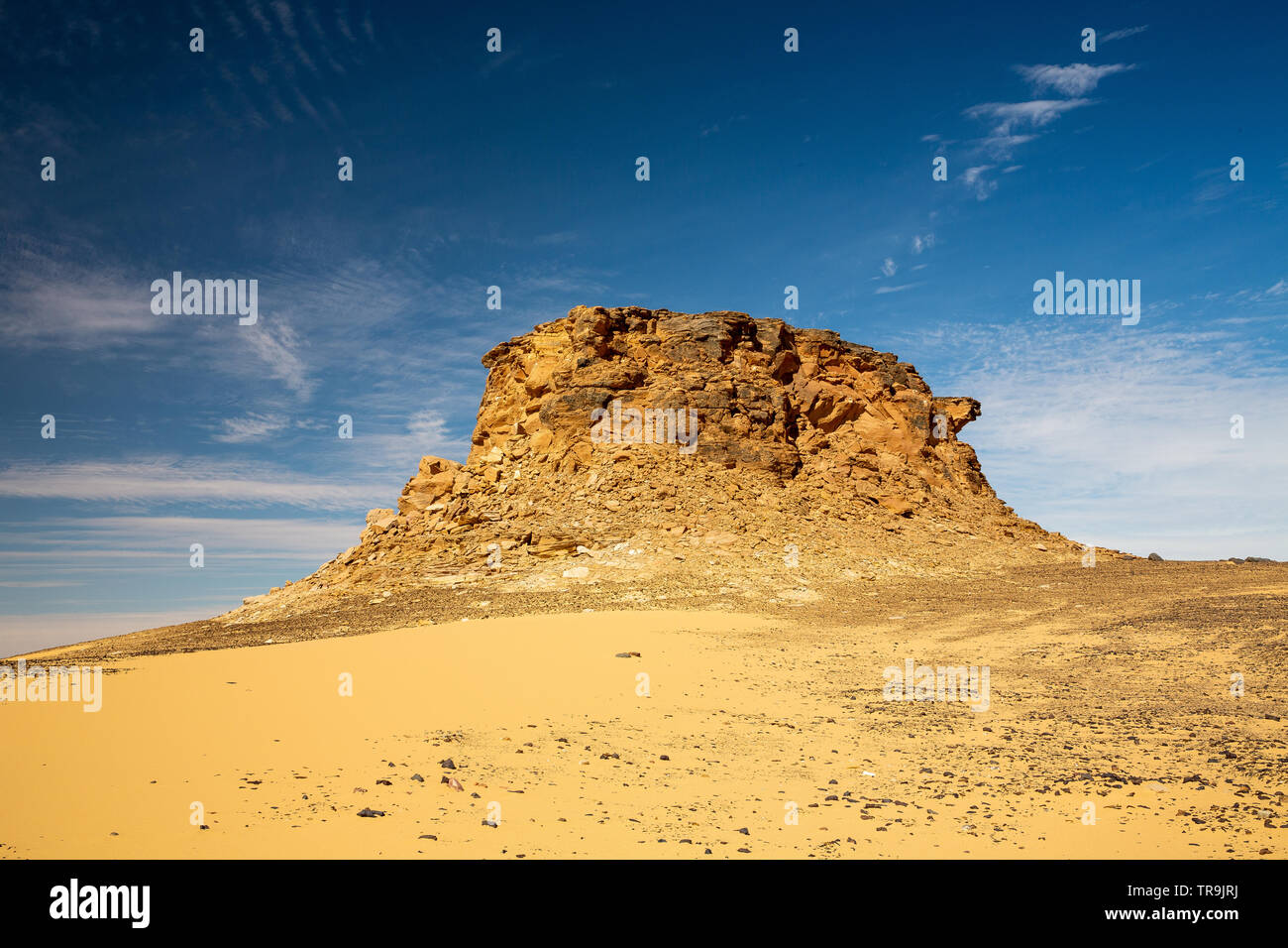 Jebel Peak, a crumbling sandstone mountain, isolated an surrounded by the flat western desert of sudan with blue sky and white cloud formations Stock Photo