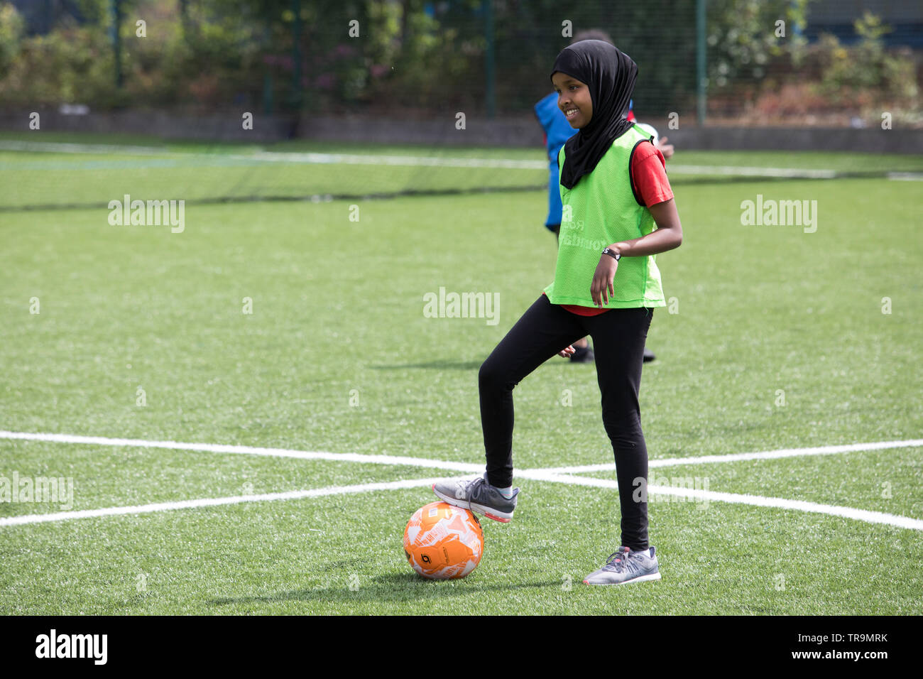 Muslim girl playing football on an astroturf training pitch. Wearing hijab (headscarves). Stock Photo