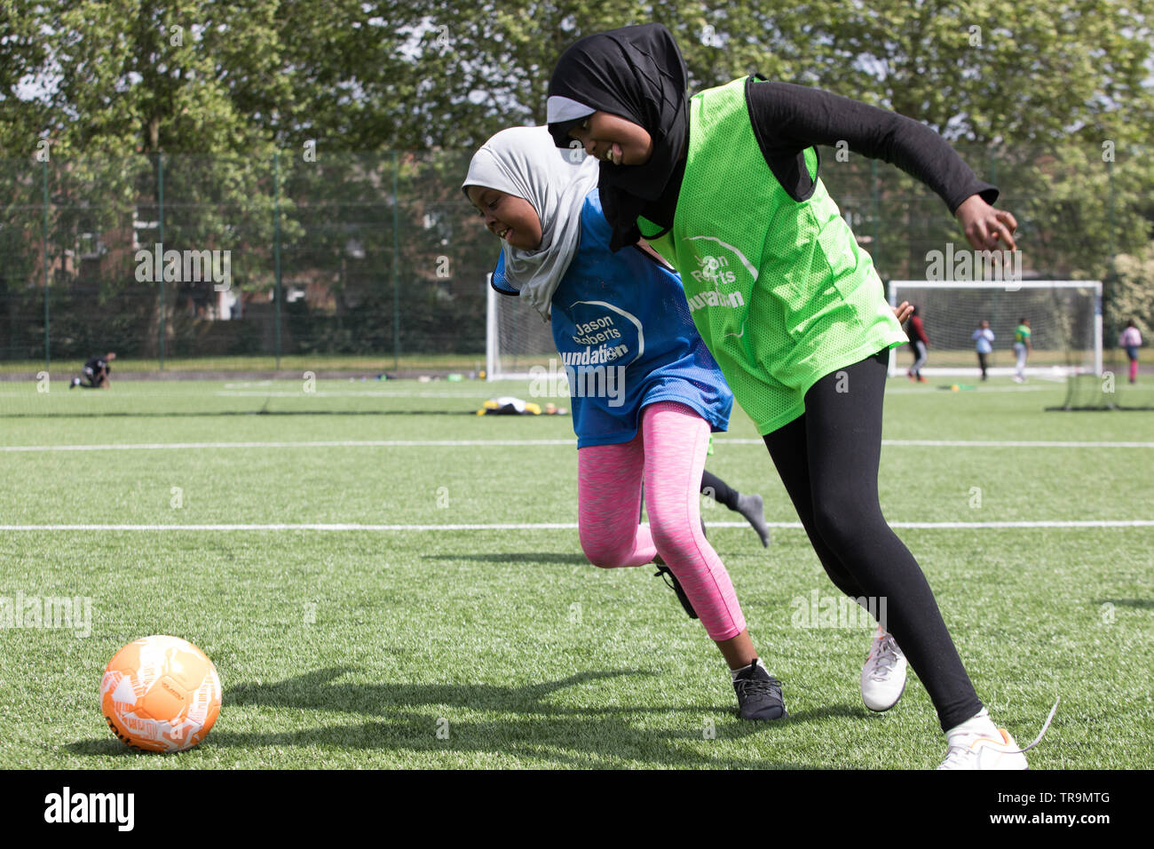 Muslim girls playing football on an astroturf training pitch. They are wearing hijabs (headscarves). Stock Photo
