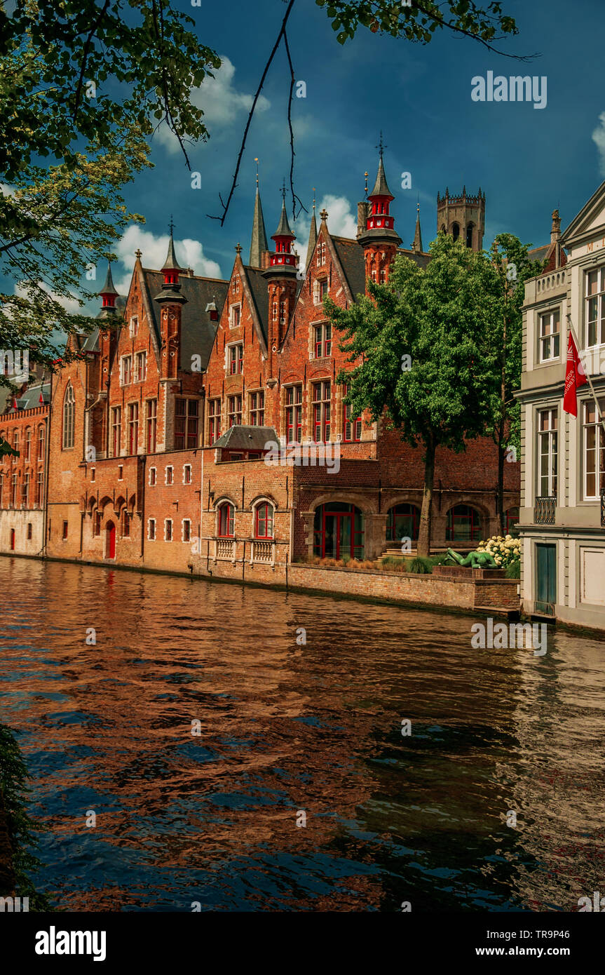 Trees and brick buildings on the canal edge in a sunny day at Bruges. Charming town with canals and old buildings in Belgium. Stock Photo