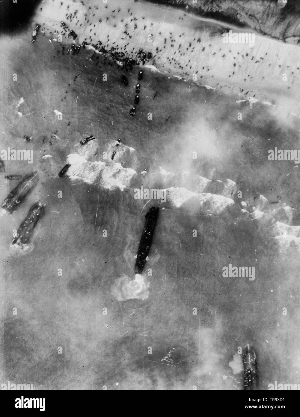 Men and assault vehicles storm the beaches of Normandy as allied landing craft make a dent in Germany's West Wall on June 6, 1944. As wave after wave of landing craft unload their cargo, men move inland and vehicles surge up the roads. Note the men swarming over the beaches. June 6, 1944 Stock Photo