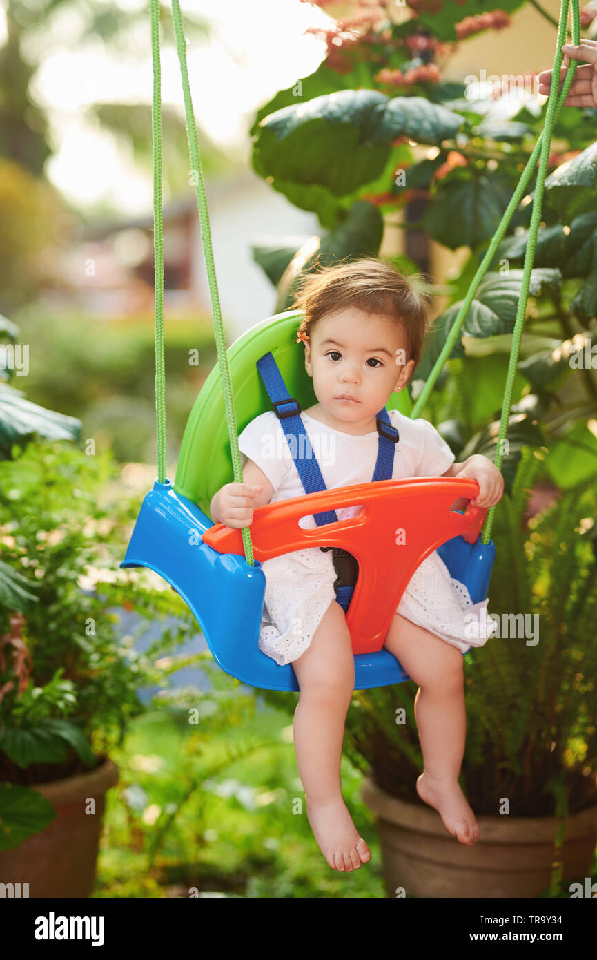 Little baby girl portrait sit on swings in bright sunny day Stock Photo